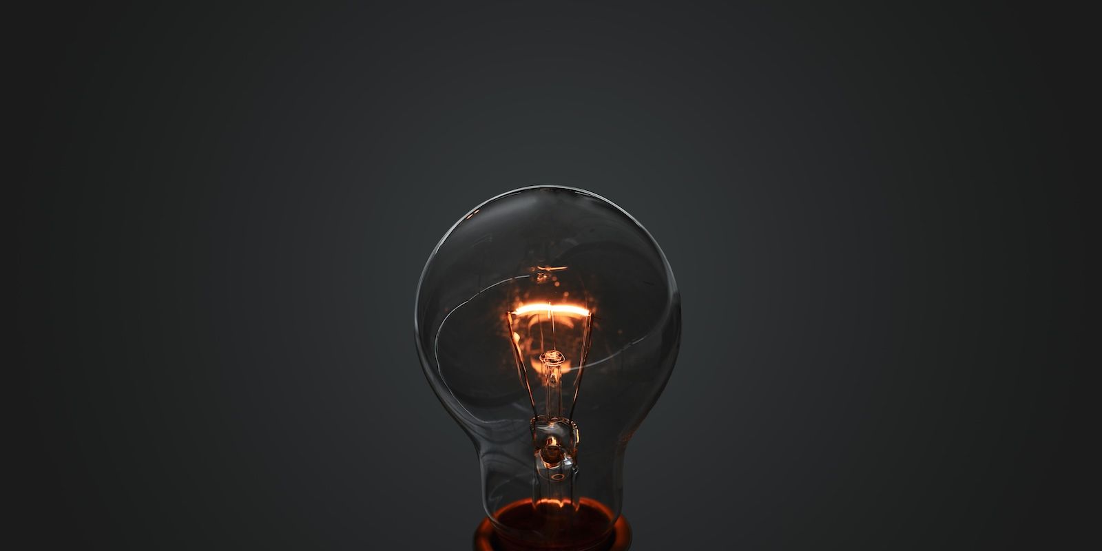 A photo of an incandescent light bulb with lit filament over gray gradient background.