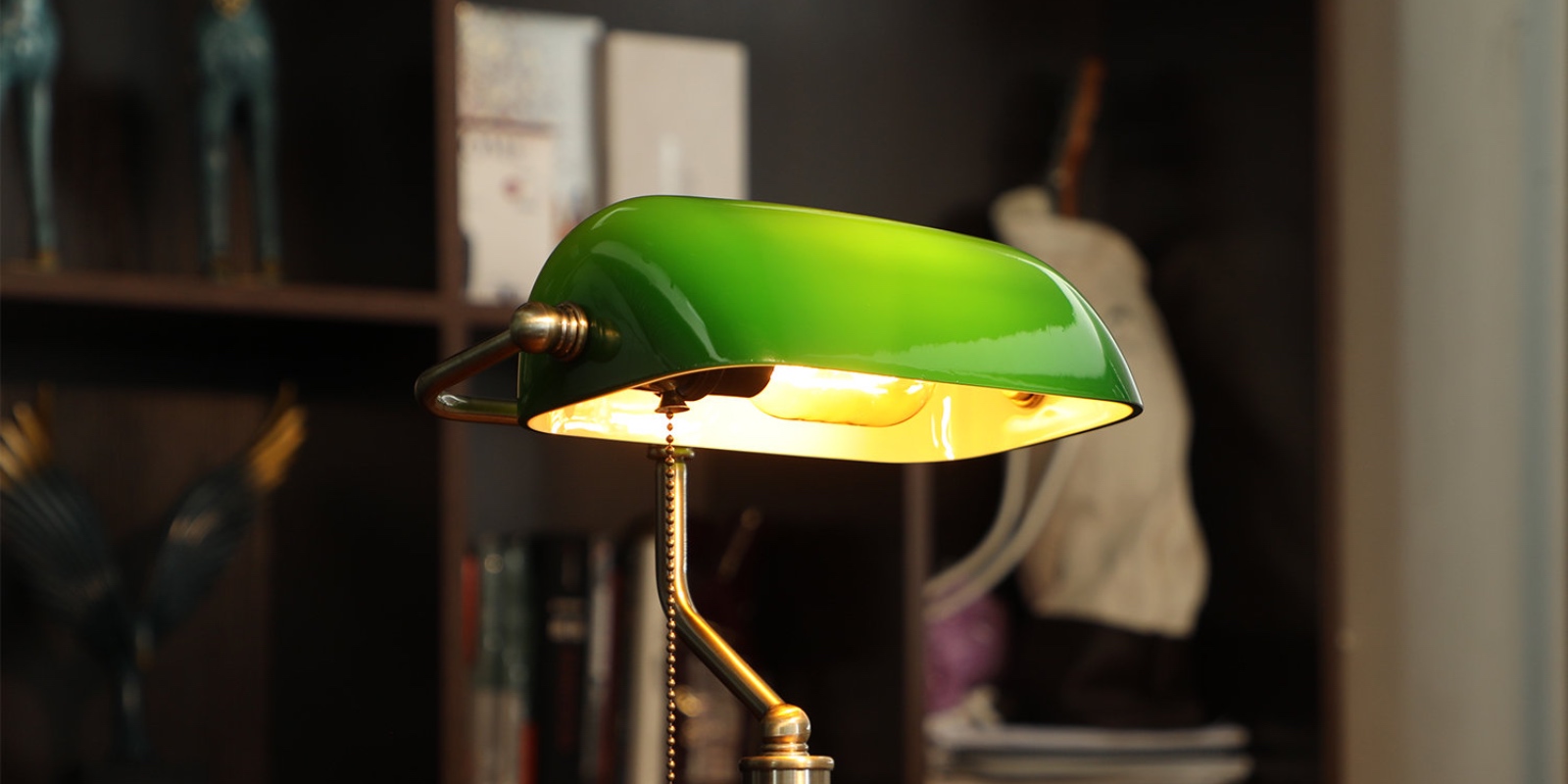 A photo of an antique green lawyer's aka banker's lamp with a brass base and shelving in the background